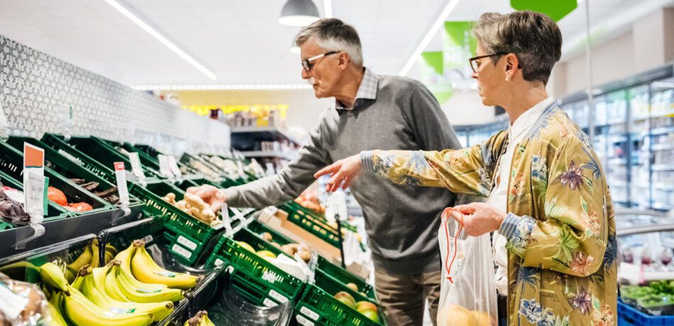 An older couple with glasses shopping for fresh produce in the grocery store.