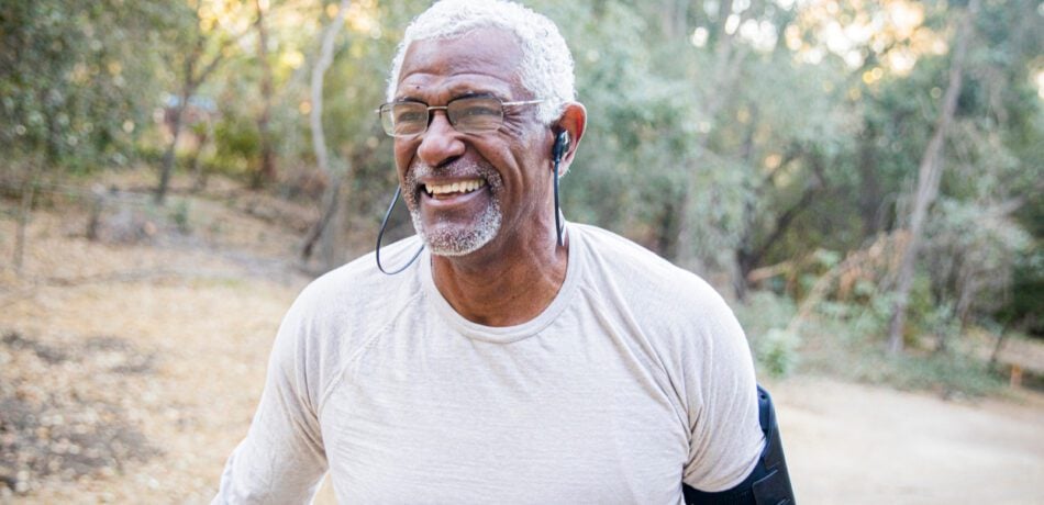 Older man in white shirt on a hiking trail smiling while exercising.