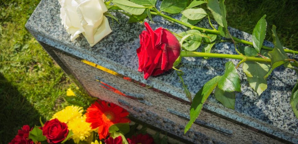 White and red roses sit on top of gray granite headstone in a cemetery with other flowers around it.