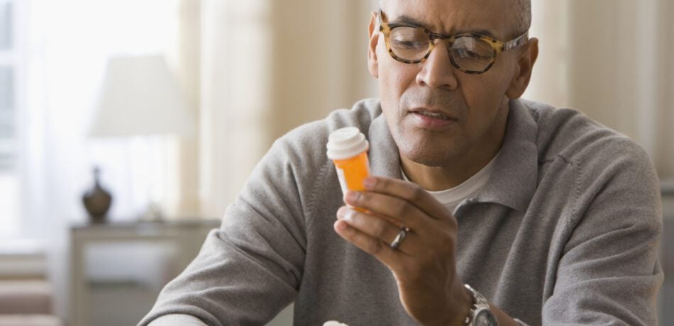 Man wearing glasses looking at a medication bottle.
