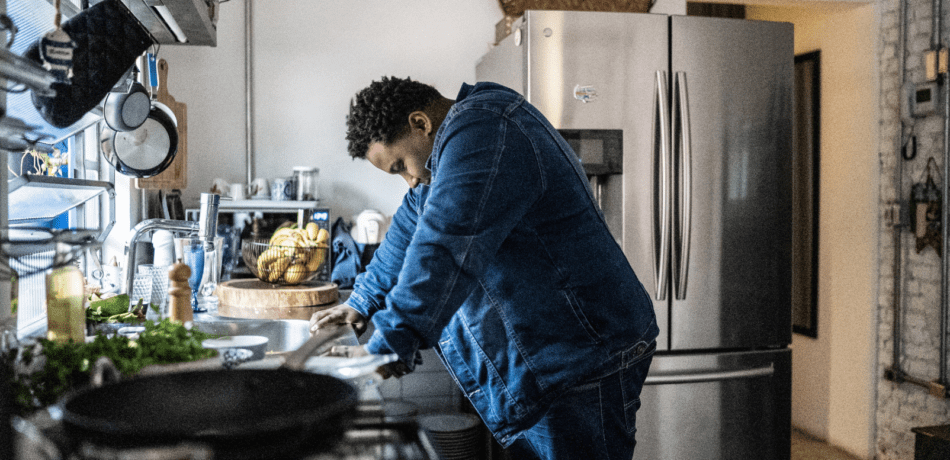 Man in jean outfit standing with head down over his kitchen sink looking depressed.