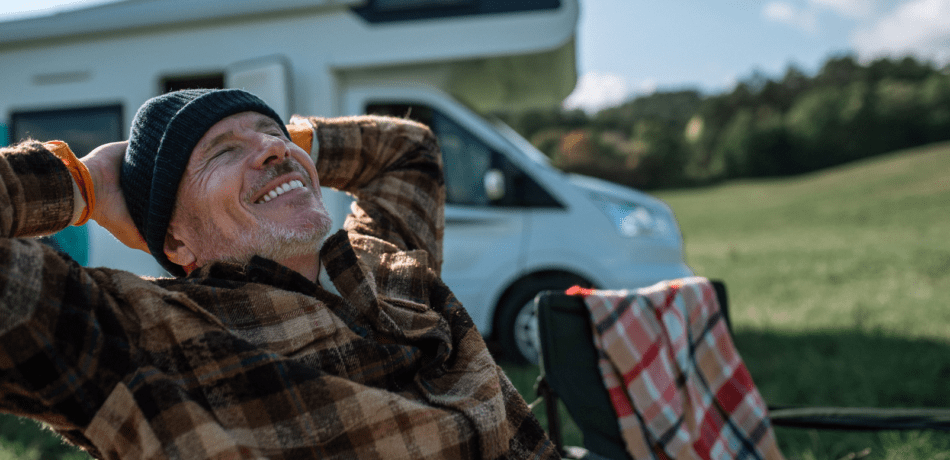 Older man smiling sitting in front of an RV.