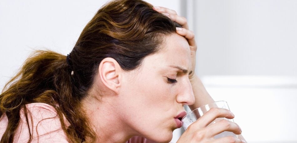 woman looking pained drinking a glass of water