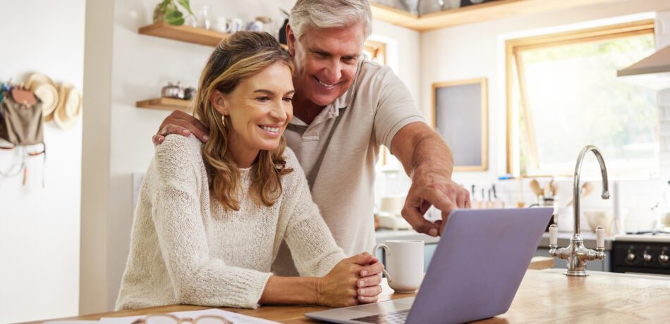 Middle aged couple smiling looking at a laptop at their kitchen counter.