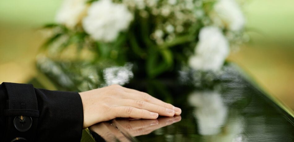 Close up of female hand on coffin with white flowers in background.