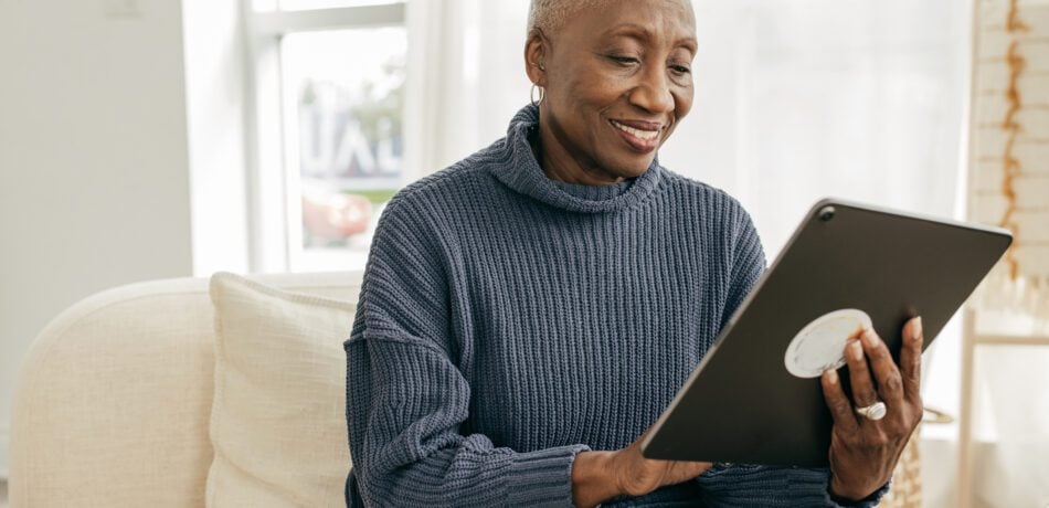 Senior woman holding a tablet while sitting on a couch smiling.