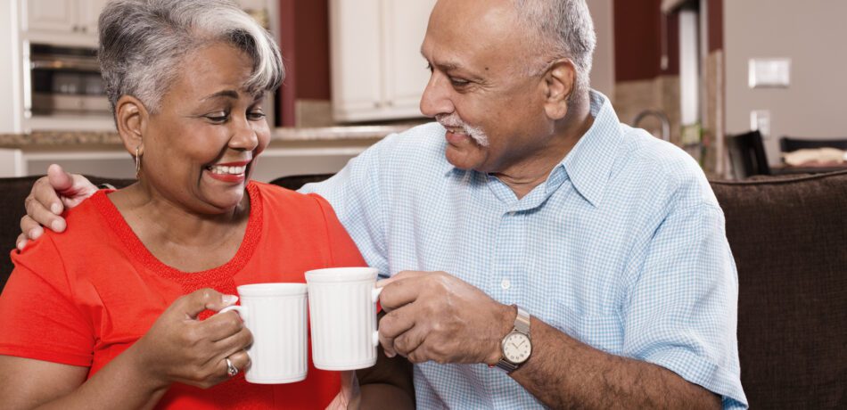 Happy senior adult couple at home enjoying cups of coffee.