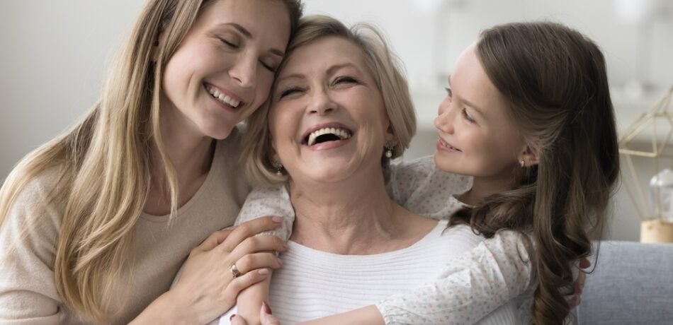 Three generations, a grandmother, daughter and granddaughter sitting and laughing on a couch together.