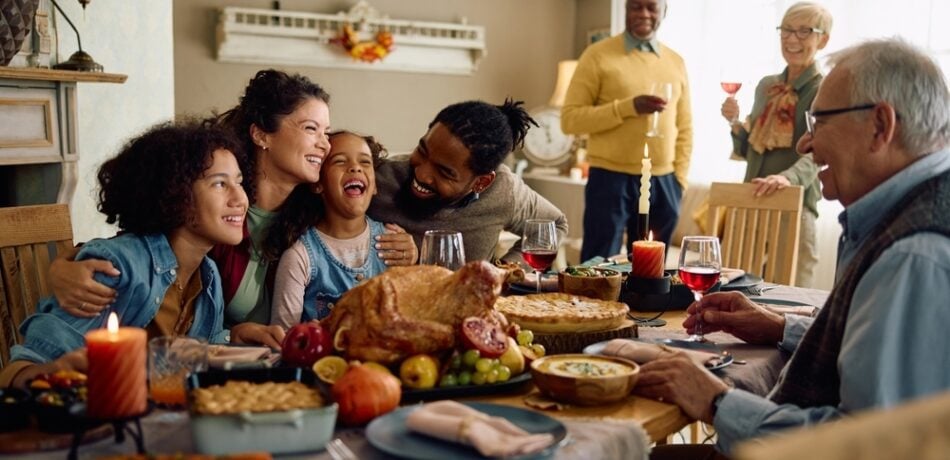 Happy multiracial parents and their kids laughing during family meal on Thanksgiving in dining room.