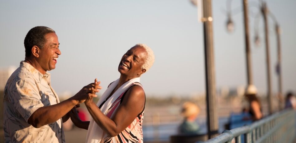 An older couple dances on a pier.