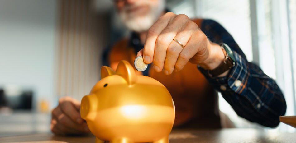 Senior man putting coins, money into a piggy bank.