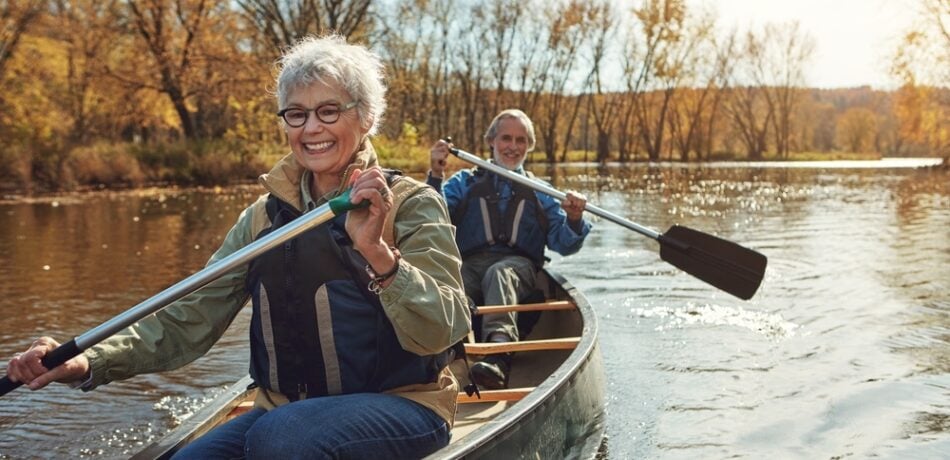 An older couple rows a canoe down a river.