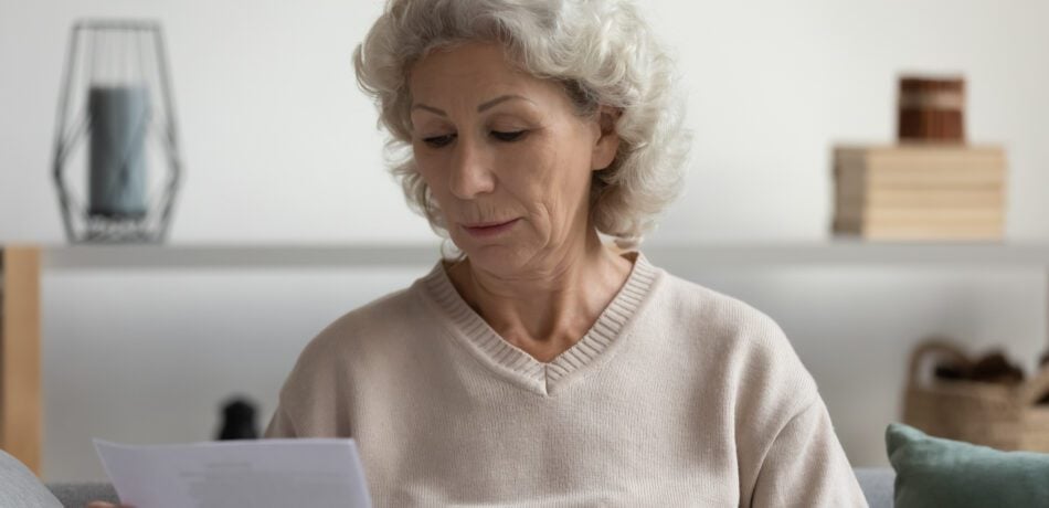 Mature woman looking down at a letter she received in the mail with a serious look on her face.