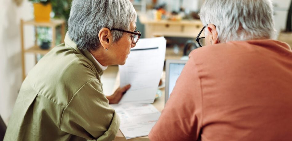 Rear view of casually clothed senior couple going over paperwork at home.