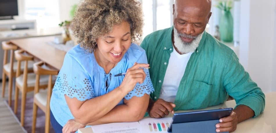 An older man uses a tablet as his wife reviews papers.