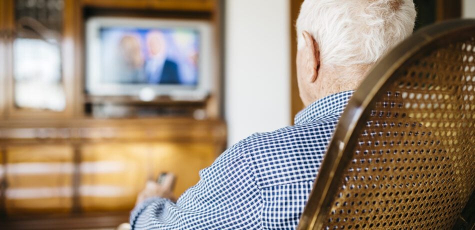 Back view of senior man sitting in his rocker watching television.