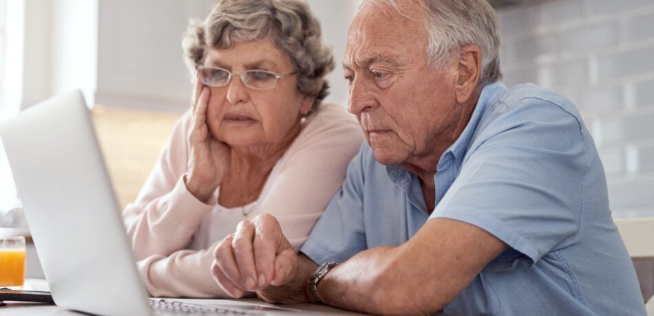 Elderly couple looking concerned as they work on their laptop.