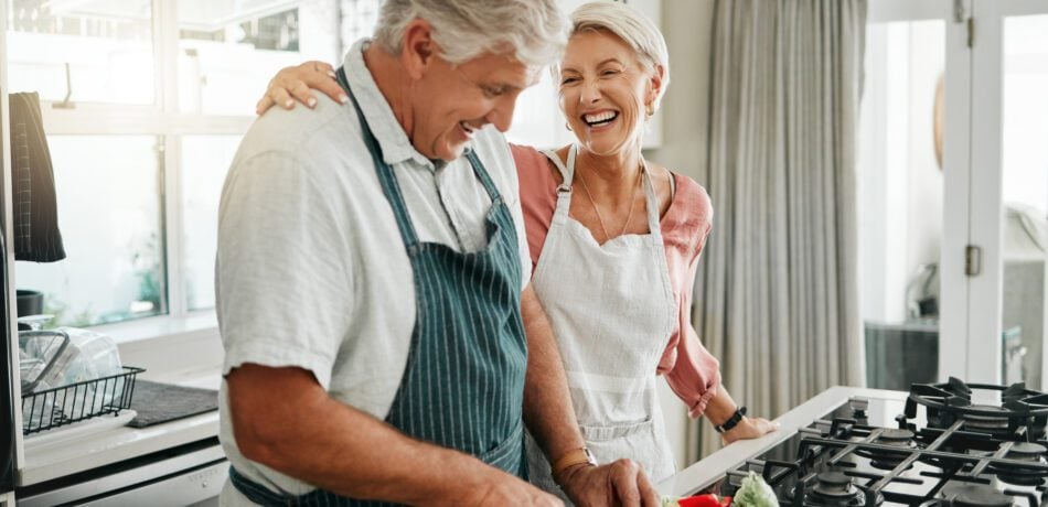 Senior couple prepping vegetables in the kitchen while laughing and enjoying each others company.