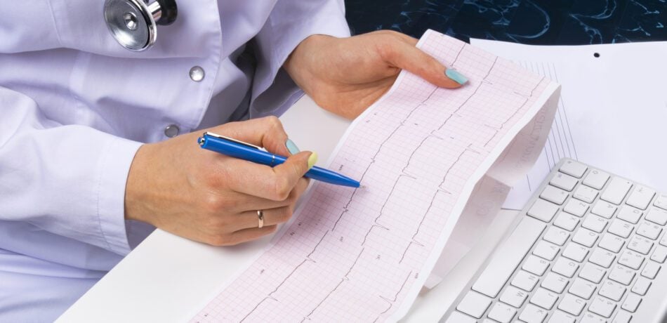 Electrocardiogram (EKG) result in hand of doctor with a computer keyboard in view.