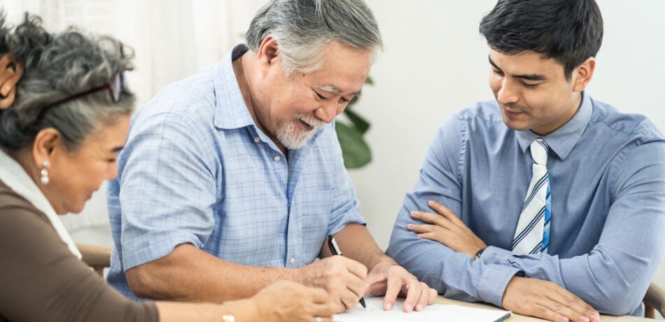 A couple signs documents as a representative looks on.