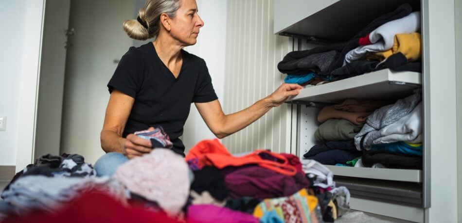 Middle aged woman sitting on floor in front of a set of drawers decluttering and organizing her closet.