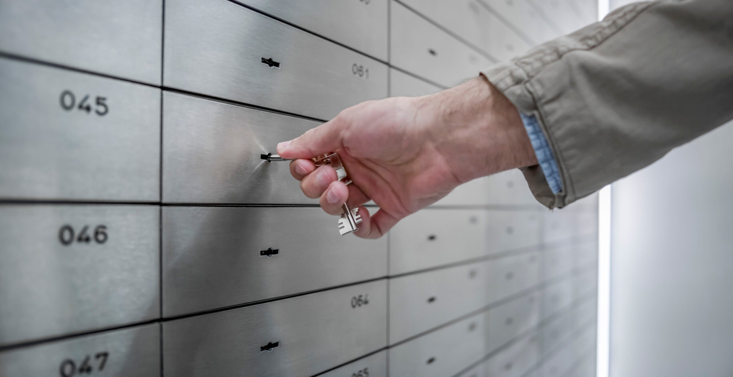 Man's hand holding a key in the lock of a safe deposit box at a bank.