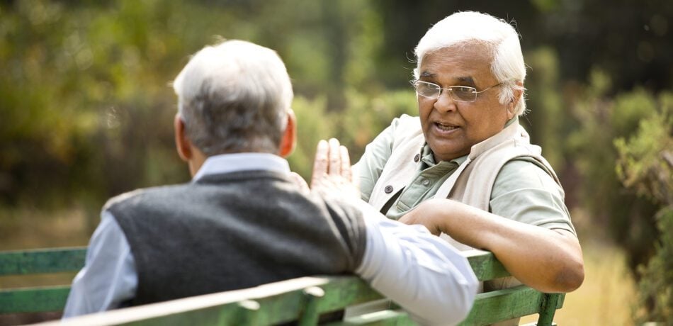 Two retired elderly men sitting on a park bench chatting and enjoying each other's company.