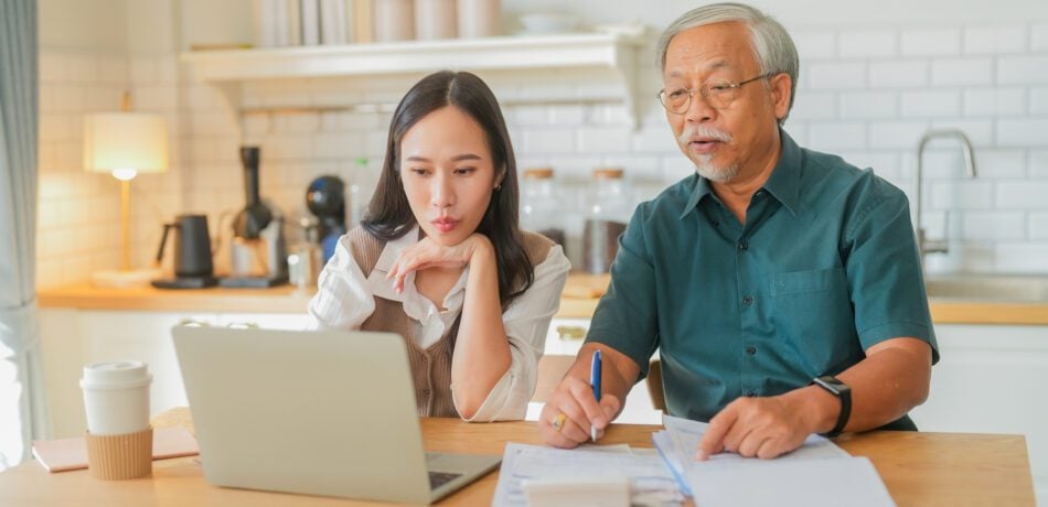 An adult daughter and elderly father review finances and estate planning matters in their home.
