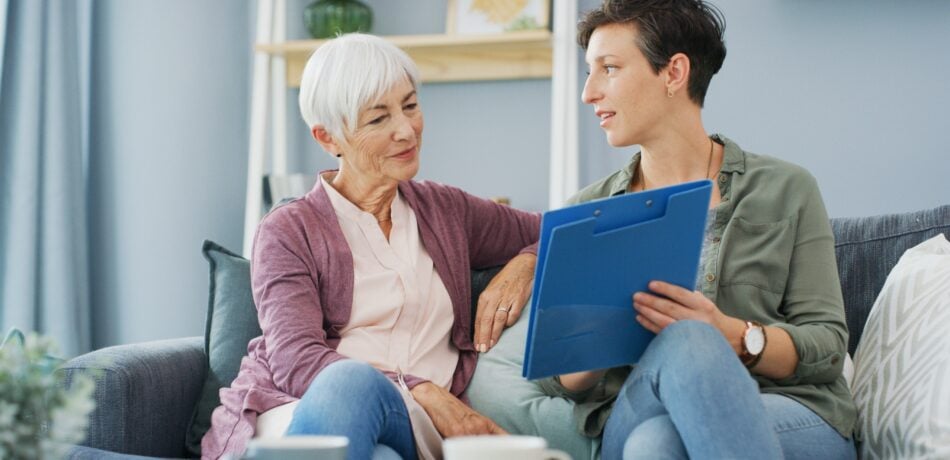 Adult woman explaining something from a clipboard to an older woman.